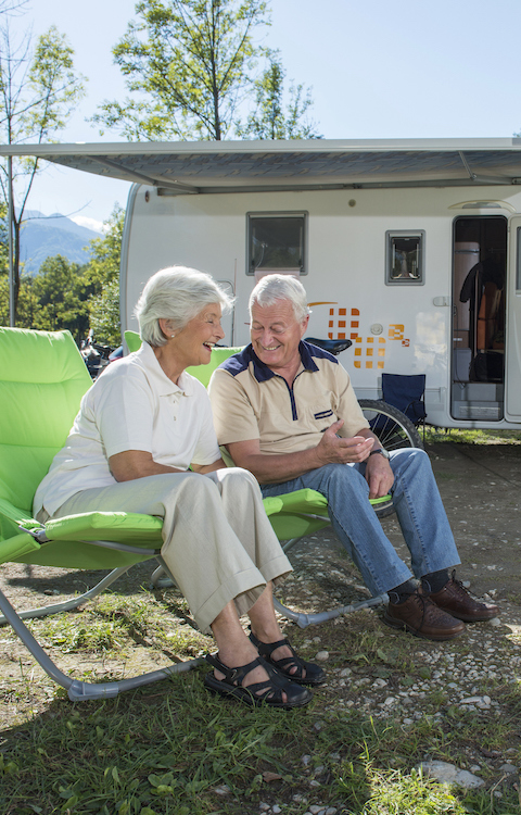Senior couple sitting in front of camper van and having fun