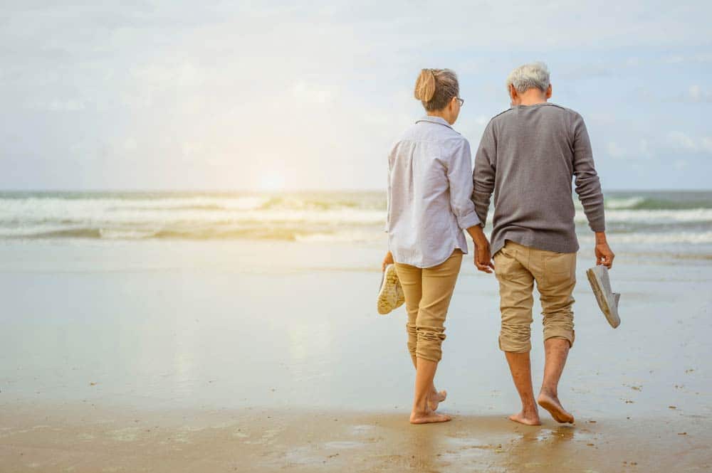 Senior Couple Walking On The Beach Holding Hands